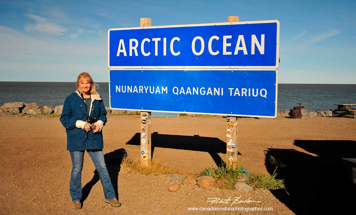Donna in front the Arctic ocean sign in Tuktoyaktuk by Robert Berdan 