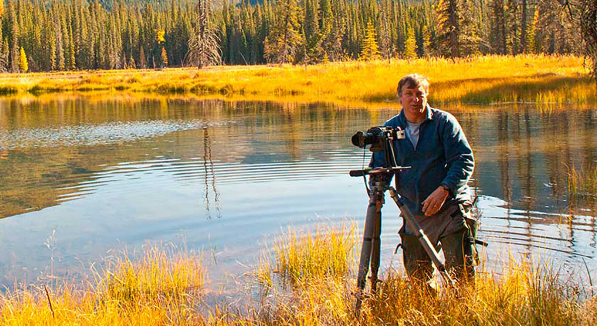 Robert Berdan in a pond with waders taking photos by Halle Flygare